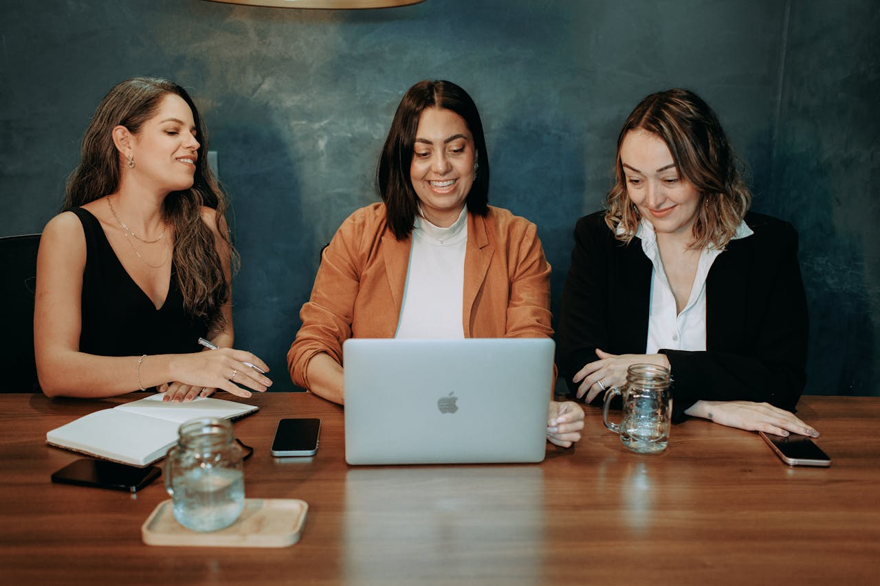 Mastering the First Impression: Your intriguing post title goes here Three women engaged in a business meeting around a laptop, showcasing teamwork and collaboration.